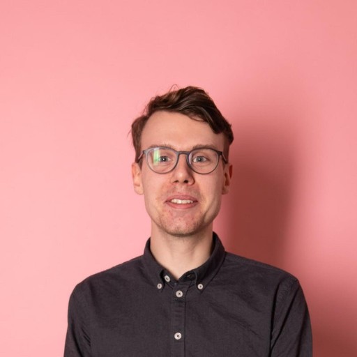Profil picture from Oscar, short brown hair, brown glasses, brown shirt in front of a rose wall